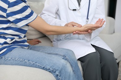 Photo of Doctor checking woman's pulse with fingers on sofa indoors, closeup