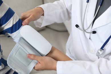 Photo of Doctor checking woman's heart rate and blood pressure via sphygmomanometer on sofa indoors, closeup