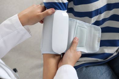 Photo of Doctor checking woman's heart rate and blood pressure via sphygmomanometer on sofa indoors, closeup
