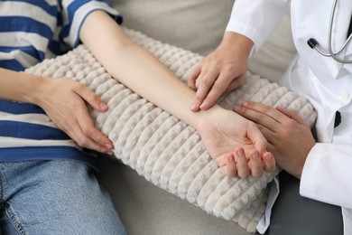 Photo of Doctor checking woman's pulse with fingers on sofa indoors, closeup