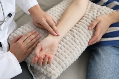 Photo of Doctor checking woman's pulse with fingers on sofa indoors, closeup