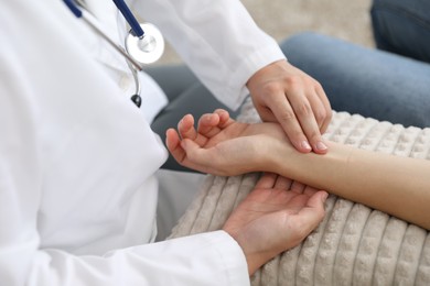Photo of Doctor checking woman's pulse with fingers on sofa indoors, closeup