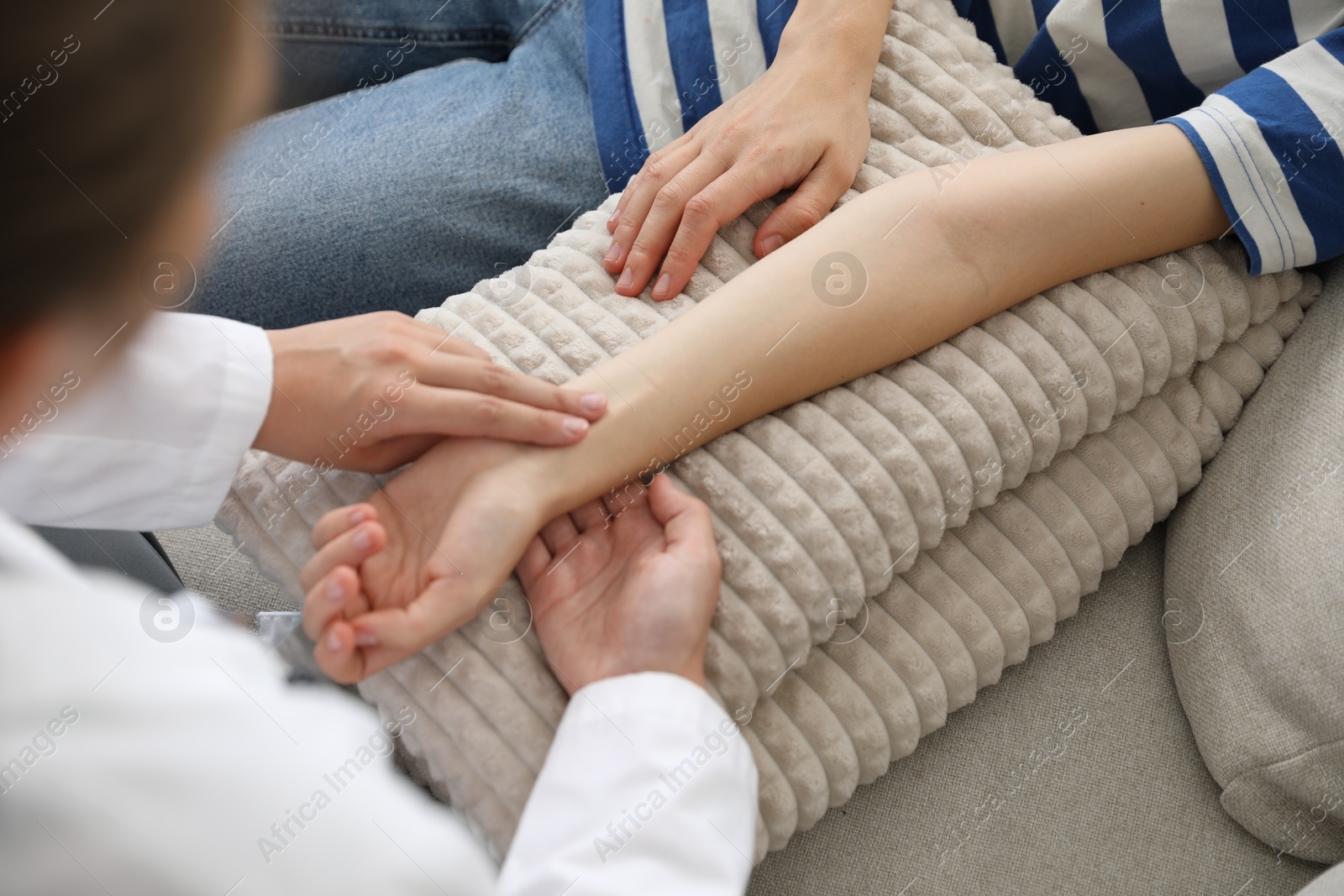 Photo of Doctor checking woman's pulse with fingers on sofa indoors, closeup