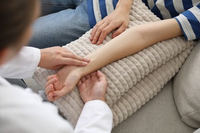 Photo of Doctor checking woman's pulse with fingers on sofa indoors, closeup
