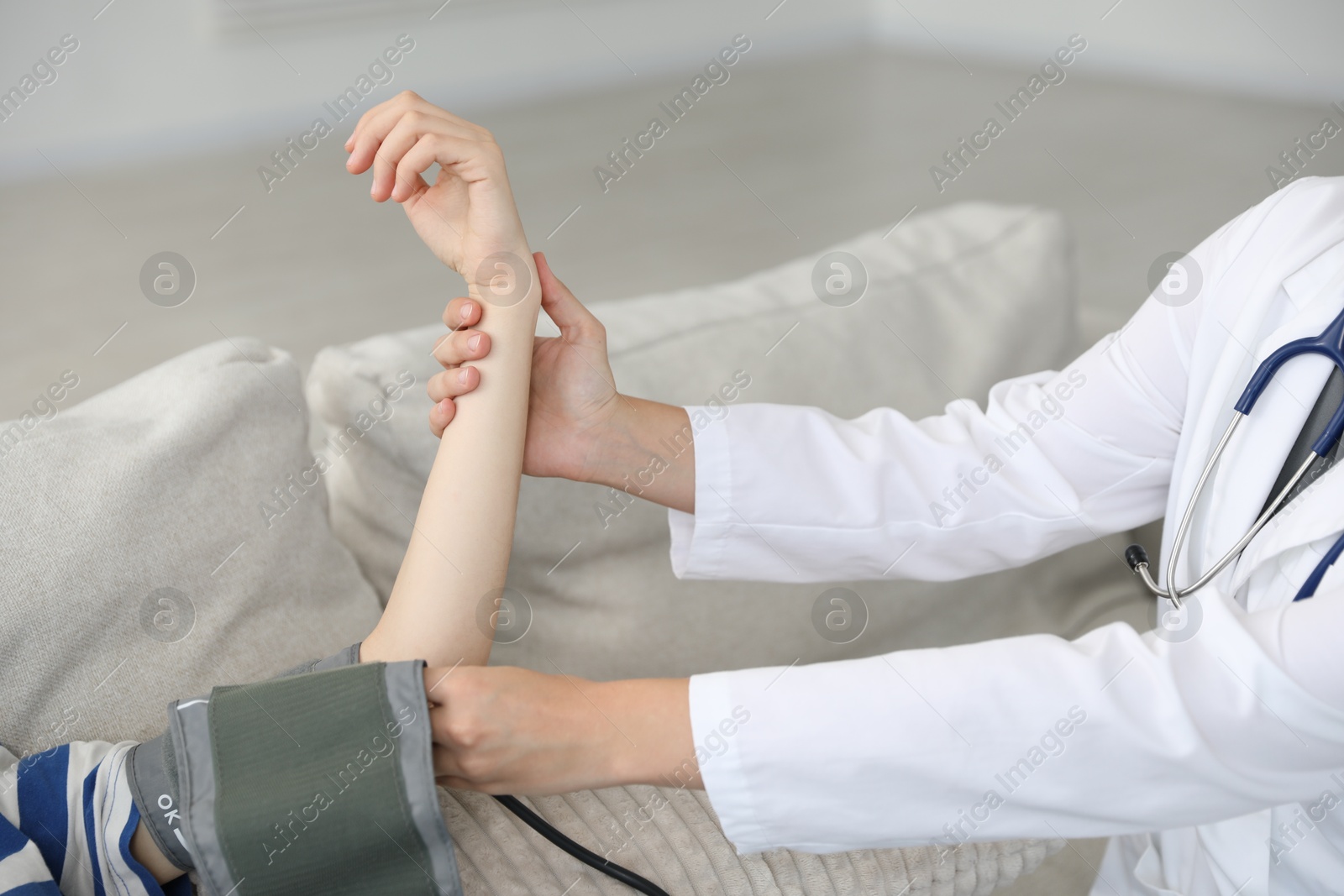 Photo of Doctor checking woman's heart rate and blood pressure via sphygmomanometer on sofa indoors, closeup