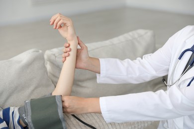 Photo of Doctor checking woman's heart rate and blood pressure via sphygmomanometer on sofa indoors, closeup