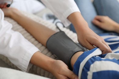 Photo of Doctor checking woman's heart rate and blood pressure via sphygmomanometer on sofa indoors, closeup