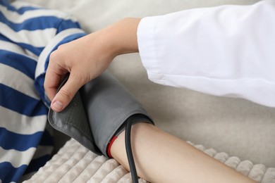 Photo of Doctor checking woman's heart rate and blood pressure via sphygmomanometer on sofa indoors, closeup