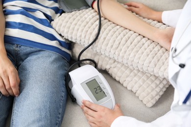 Photo of Doctor checking woman's heart rate and blood pressure via sphygmomanometer on sofa indoors, closeup