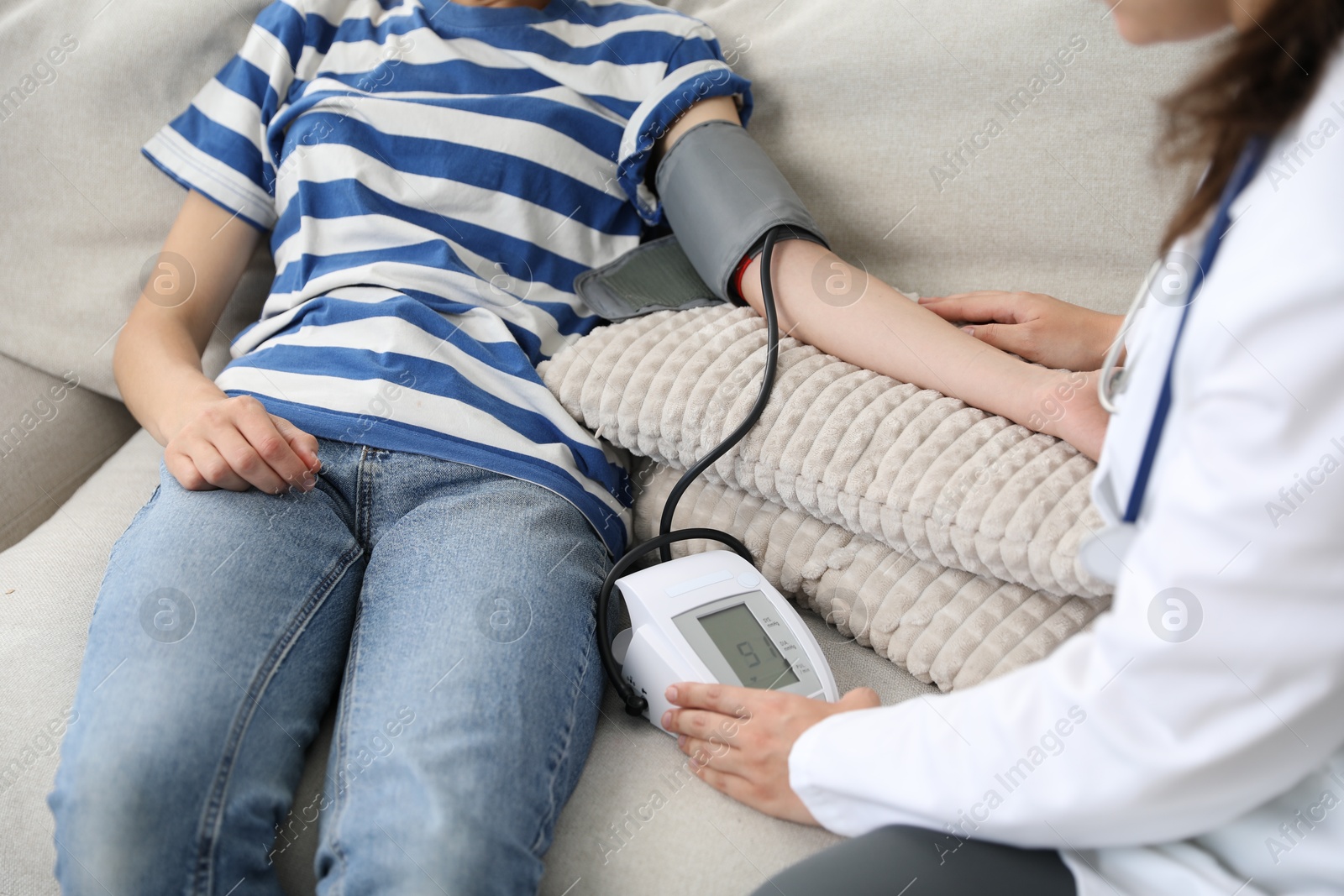 Photo of Doctor checking woman's heart rate and blood pressure via sphygmomanometer on sofa indoors, closeup