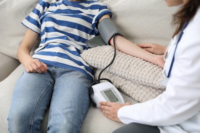 Photo of Doctor checking woman's heart rate and blood pressure via sphygmomanometer on sofa indoors, closeup