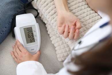 Photo of Doctor checking woman's heart rate and blood pressure via sphygmomanometer on sofa indoors, closeup