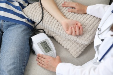 Photo of Doctor checking woman's heart rate and blood pressure via sphygmomanometer on sofa indoors, closeup