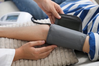 Photo of Doctor checking woman's heart rate and blood pressure via sphygmomanometer on sofa indoors, closeup