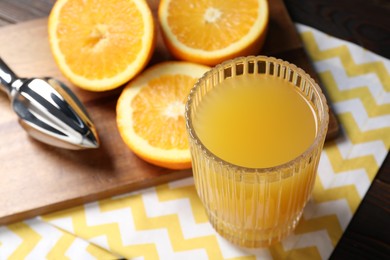 Photo of Freshly squeezed orange juice, fruits, juicer and towel on wooden table, closeup