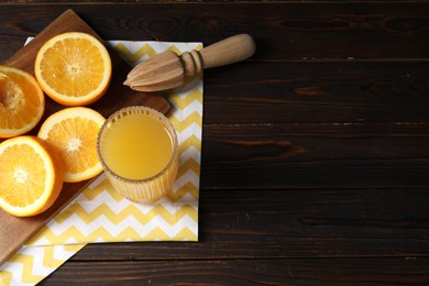Photo of Freshly squeezed orange juice, fruits, juicer and towel on wooden table, above view. Space for text