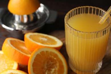 Photo of Freshly squeezed orange juice, fruits and juicer on wooden table, closeup