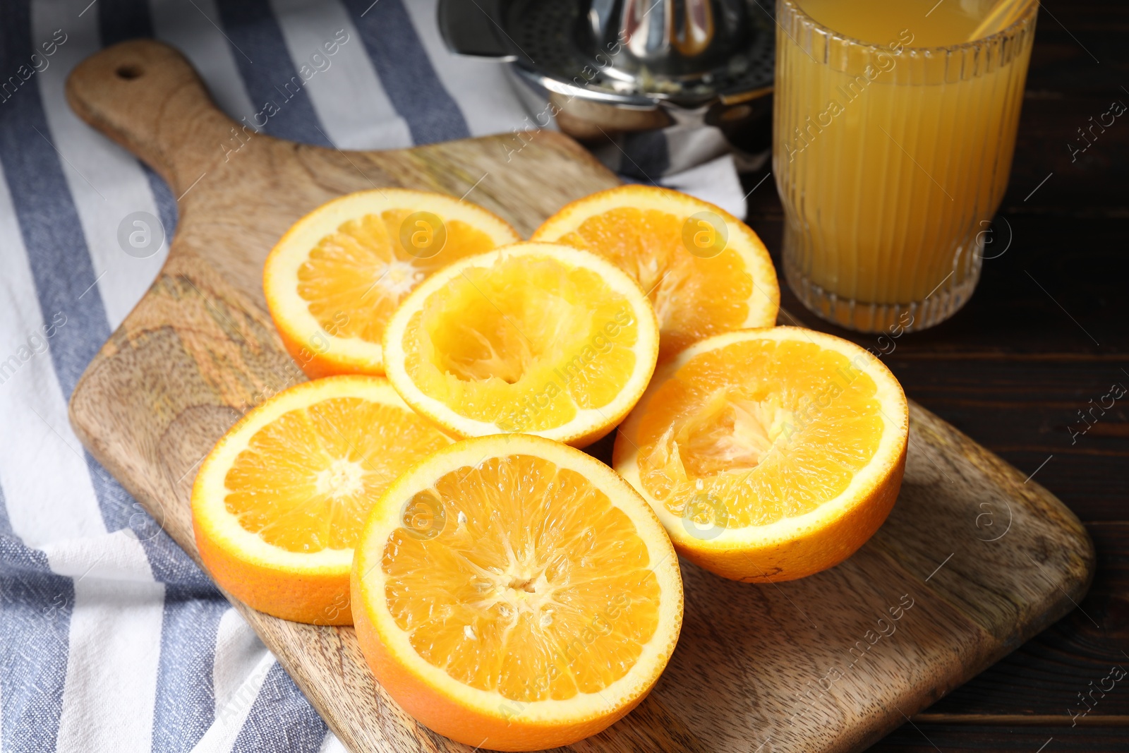 Photo of Freshly squeezed orange juice, fruits, juicer and towel on wooden table, closeup