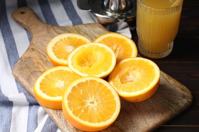 Photo of Freshly squeezed orange juice, fruits, juicer and towel on wooden table, closeup