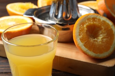 Photo of Freshly squeezed orange juice, fruits and juicer on wooden table, selective focus