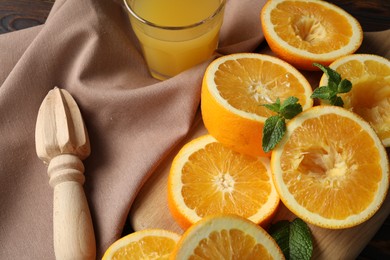 Photo of Freshly squeezed orange juice, fruits, mint, juicer and towel on wooden table, closeup