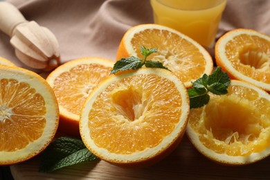 Photo of Squeezed oranges with mint, juicer and towel on table, closeup