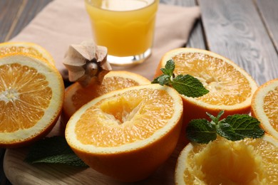 Photo of Freshly squeezed orange juice, fruits, mint, juicer and towel on wooden table, closeup