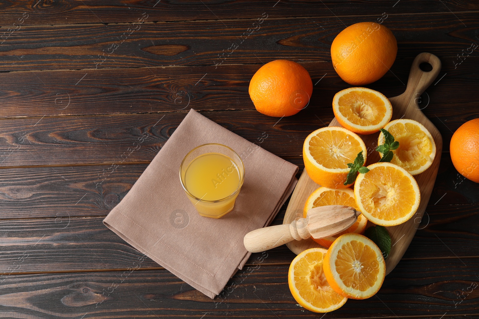 Photo of Freshly squeezed orange juice, fruits, mint, juicer and towel on wooden table, above view. Space for text
