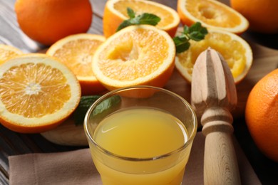 Photo of Freshly squeezed orange juice, fruits with mint, juicer and towel on table, closeup