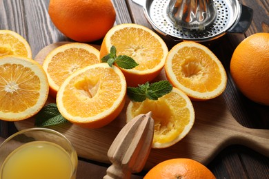 Photo of Freshly squeezed orange juice, fruits with mint and juicer on wooden table, closeup