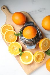 Photo of Squeezer with oranges and mint on white table, flat lay. Making fresh juice