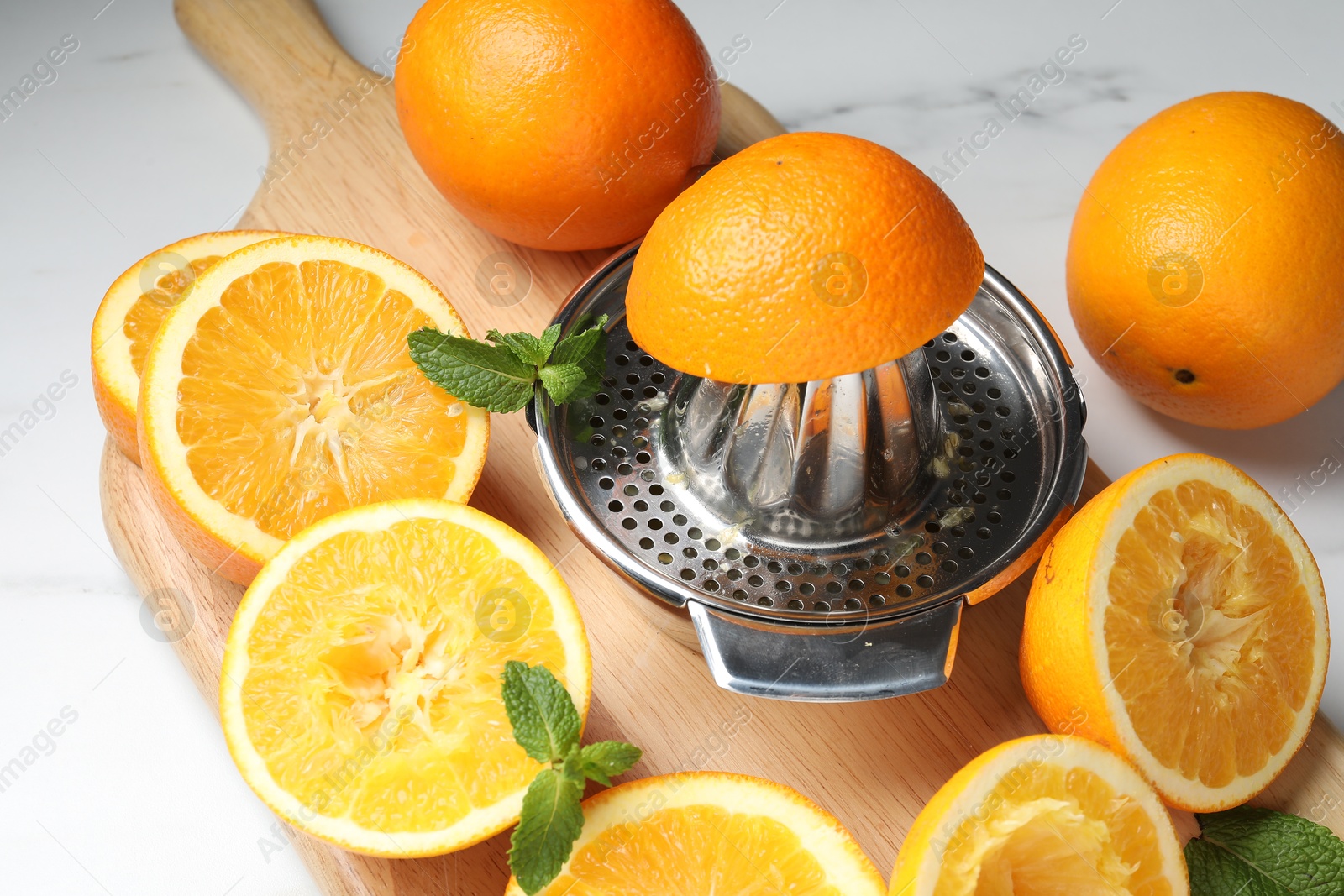 Squeezer with oranges and mint on white table, closeup. Making fresh juice Photo of Squeezer with oranges and mint on white table, closeup. Making fresh juice