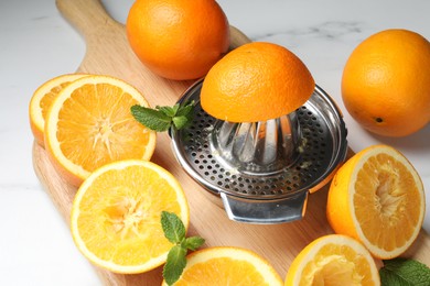 Photo of Squeezer with oranges and mint on white table, closeup. Making fresh juice