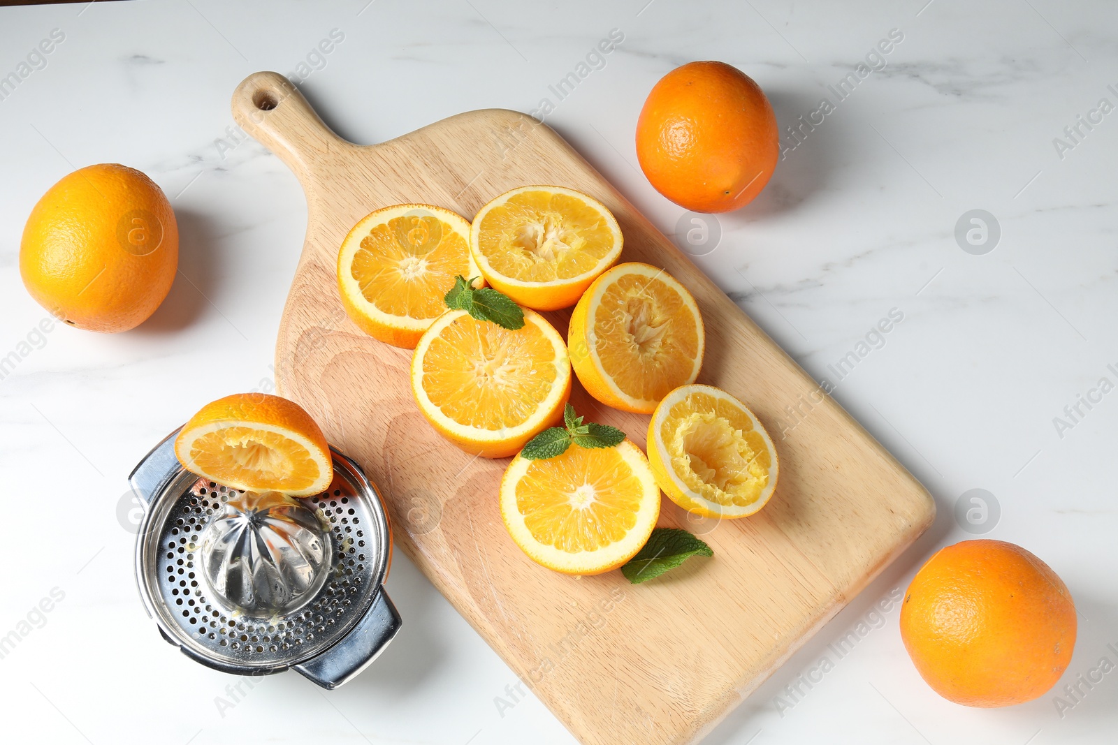 Squeezer with oranges and mint on white table, flat lay. Making fresh juice Photo of Squeezer with oranges and mint on white table, flat lay. Making fresh juice