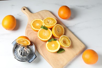 Photo of Squeezer with oranges and mint on white table, flat lay. Making fresh juice