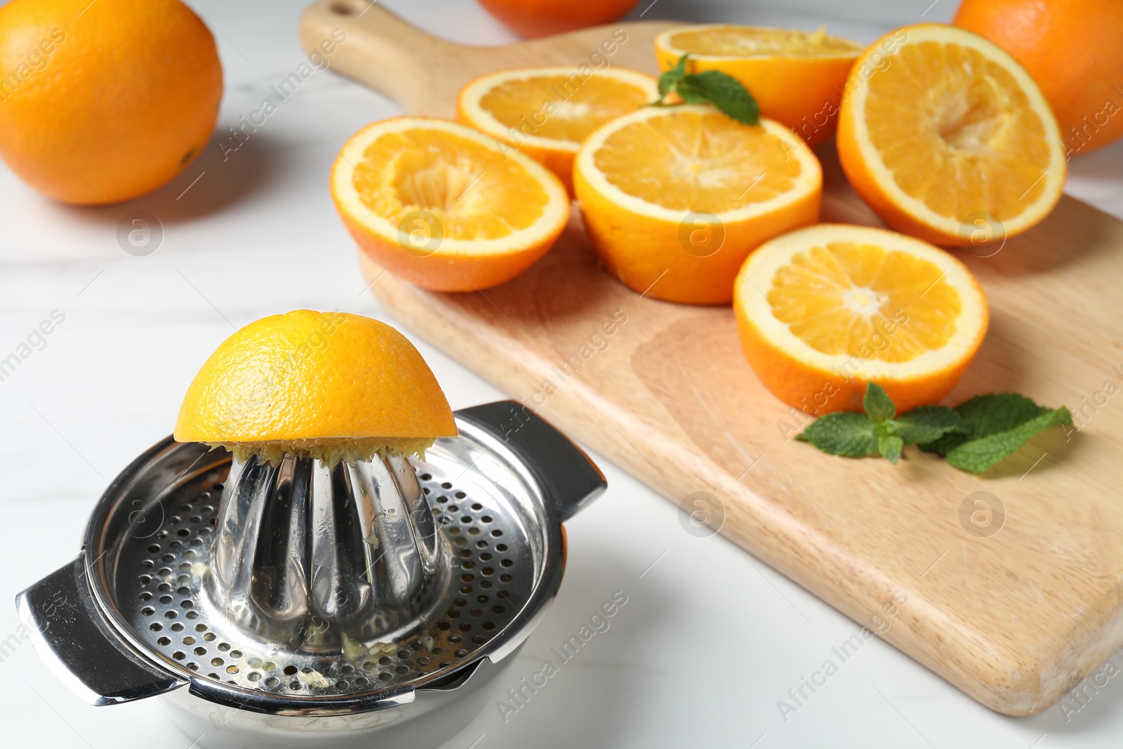 Squeezer with oranges and mint on white table, closeup. Making fresh juice Photo of Squeezer with oranges and mint on white table, closeup. Making fresh juice