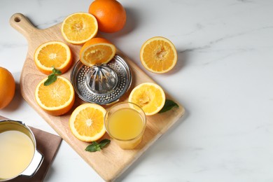 Photo of Squeezer with oranges, mint and fresh juice on white table, flat lay. Space for text