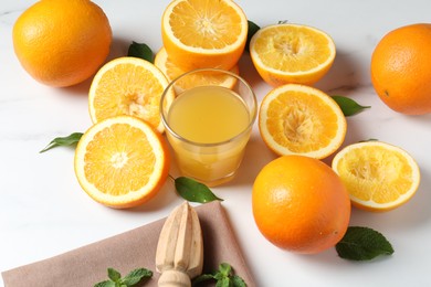 Photo of Freshly squeezed orange juice, fruits and juicer on white table, closeup