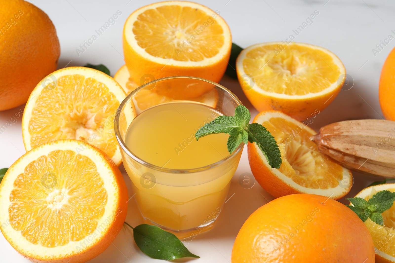 Photo of Freshly squeezed orange juice, fruits and juicer on white table, closeup
