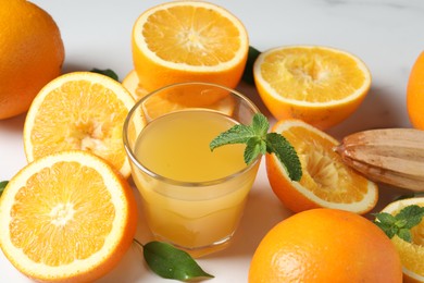 Photo of Freshly squeezed orange juice, fruits and juicer on white table, closeup