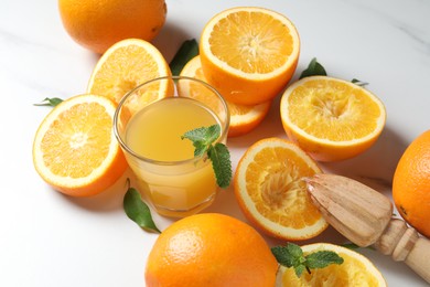 Photo of Freshly squeezed orange juice, fruits and juicer on white table, closeup