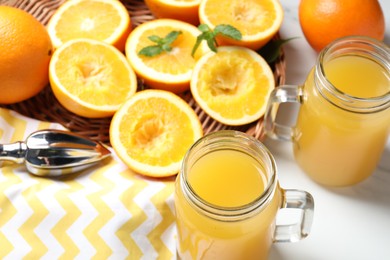 Photo of Freshly squeezed orange juice, fruits and juicer on white table, closeup