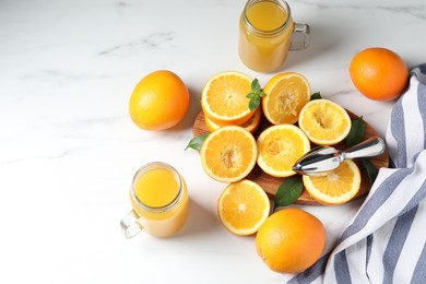 Photo of Freshly squeezed orange juice, fruits, juicer and towel on white table, flat lay. Space for text