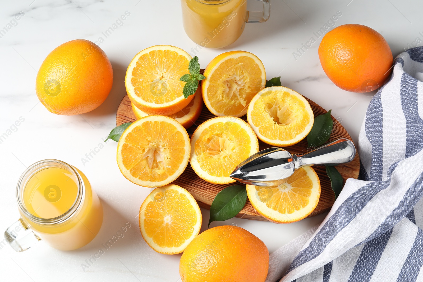 Photo of Freshly squeezed orange juice, fruits, juicer and towel on white table, flat lay