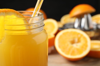 Photo of Freshly squeezed orange juice in mason jar and fruits on table, selective focus