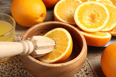 Photo of Squeezed oranges with juicer and glass of juice on wooden table, closeup