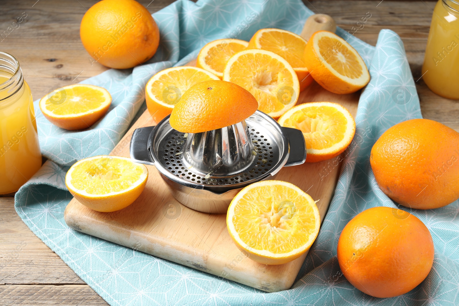 Photo of Freshly squeezed orange juice, fruits, juicer and towel on wooden table