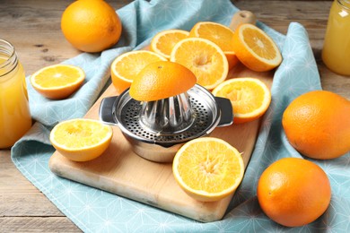 Photo of Freshly squeezed orange juice, fruits, juicer and towel on wooden table