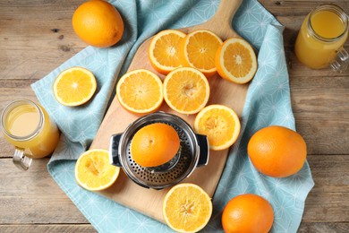 Photo of Freshly squeezed orange juice, fruits, juicer and towel on wooden table, flat lay