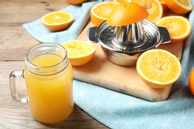 Photo of Freshly squeezed orange juice, fruits, juicer and towel on wooden table, closeup
